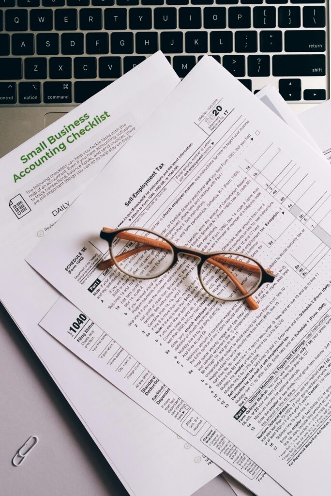 pexels-photo-8962456-8962456 Overhead view of tax documents and eyeglasses on a laptop keyboard, ideal for finance or accounting themes.